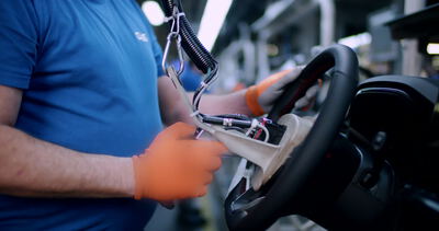 Arbeiter montiert ein Lenkrad mit freiliegender Elektronik in einer Automobilfabrik: Lenkrad, Montage
