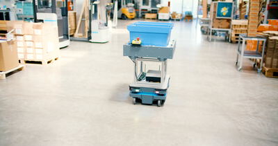 Autonomes Transportsystem mit blauer Materialbox fährt eigenständig durch ein modernes Industrielager