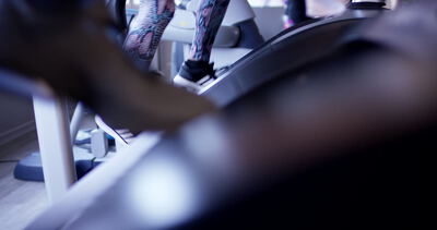 Beine einer Person in gemusterten Leggings beim Training auf einem Fitnessgerät im Studio