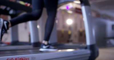 Beine und Füße einer Person beim Laufen auf einem Laufband im Fitnessstudio aus der Rückansicht
