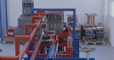 Blick auf eine industrielle Prüfanlage für Stahlseile mit gelagerten Kabelrollen im Hintergrund