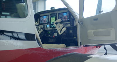 Blick durch die geöffnete Kabinentür in das moderne Cockpit eines Kleinflugzeugs mit digitalen Glascockpit-Displays
