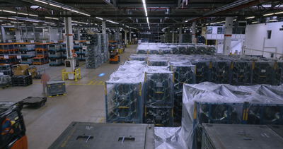 Blick in eine große Logistikhalle mit Gabelstaplern und gelagerter Ware in Transportboxen