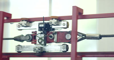 Detailaufnahme einer mechanischen Prüfvorrichtung mit eingespanntem Stahlseil in Bewegung