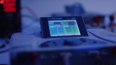 Digitales Ladegerät mit Display und Kabelverbindungen auf einem Prüfstand bei blauem Licht, Bildschirm, Messgerät und