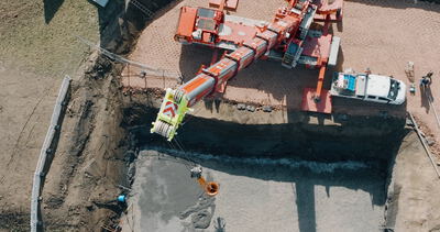 Draufsicht auf einen roten Mobilkran beim Betonieren eines Fundaments in einer Baugrube mit Betonkübel