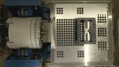 Draufsicht eines industriellen Vibrationsprüfstands mit einer metallischen Montageplatte in einer Laborhalle