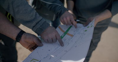 Drei Personen besprechen technische Zeichnungen einer Ausführungsplanung im Freien auf einer Baustelle