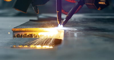 Extreme Nahaufnahme einer CNC-Brennschneidmaschine beim präzisen Schneiden einer dicken Metallplatte mit Funkenflug