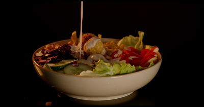 Frische Bowl mit Falafel und Gemüse wird mit Dressing verfeinert und vor schwarzem Hintergrund gedreht