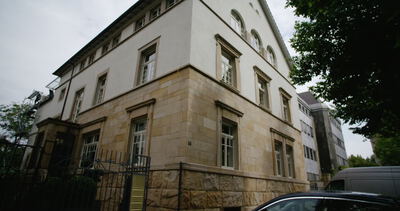 Froschperspektive von einem mehrstöckigen Wohnhaus mit Sandsteinfassade und weißem Putz an einer Straße