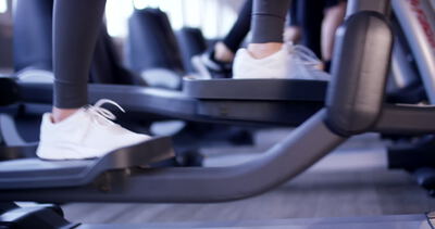 Füße in weißen Sportschuhen beim Ausdauertraining auf einem Crosstrainer im Fitnessstudio
