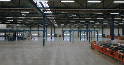 Große, weitgehend leere Industrie- oder Lagerhalle mit blauen Stahlkonstruktionen