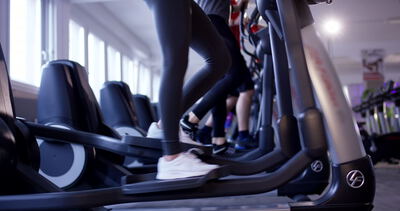 Gruppe von Personen beim synchronen Ausdauertraining auf Crosstrainern im Fitnessstudio
