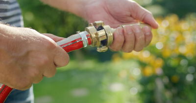 Hände eines Mannes verbinden eine goldene Messing-Schlauchkupplung an einem roten Gartenschlauch im Freien
