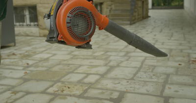 Handwerker bei der Außenreinigung mit einem Laubbläser auf einer gepflasterten Terrasse, Gebäudereinigung, Naturstein und