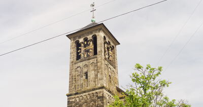 Historischer Kirchturm aus Sandstein mit goldener Turmuhr und Glockenstuhl unter bewölktem Himmel
