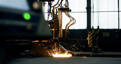 Industrielle Brennschneidmaschine im Einsatz beim thermischen Trennen einer Metallplatte mit hellem Lichtbogen: Brennschneiden, Metallbearbeitung