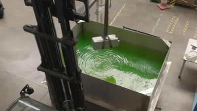 Industrieller Gabelstapler senkt einen Lithium-Ionen-Akku in ein Becken mit grüner Flüssigkeit