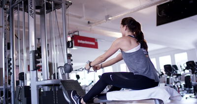 Junge Frau trainiert an der Rudermaschine im Fitnessstudio für den Rückenaufbau