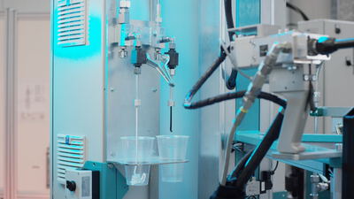 Laborgerät befüllt Plastikbecher mit einer dunklen Flüssigkeit unter blauem LED-Licht während einer manuellen Prüfung
