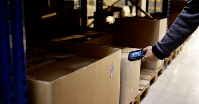 Lagerarbeiter scannt Barcode an einem Versandkarton mit einem Handscanner im Hochregallager