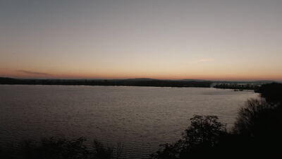 Landschaft am See während der Dämmerung mit Bäumen im Vordergrund