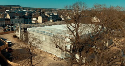 Luftaufnahme einer großen Baustelle mit eingerüstetem und planungshüllenverkleidetem Gebäude in einer Kleinstadt