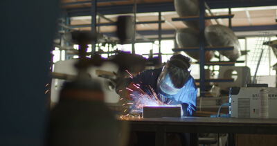 Metallarbeiter mit Schweißschutzmaske beim Schweißen von Bauteilen in einer industriellen Werkstatt