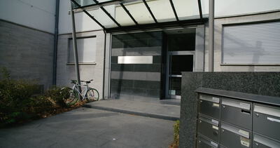 Moderner Eingangsbereich von einem Bürogebäude mit Glasvordach, Briefkastenanlage und geparkten Fahrrädern