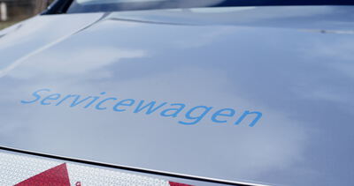 Nahaufnahme der Motorhaube eines silbernen Servicefahrzeugs mit blauem „Servicewagen“-Schriftzug