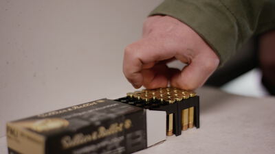 Nahaufnahme einer Hand beim Entnehmen einer einzelnen Patrone aus einer Munitionsschachtel