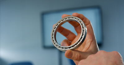 Nahaufnahme eines präzisen Kugellagers aus Metall gehalten von einer Hand in einem technischen Büro