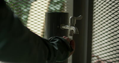 Nahaufnahme von einem Handwerker beim Anschrauben von einem Schlauchanschluss an einen Außenwasserhahn von Hand
