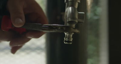 Nahaufnahme von einem Handwerker beim Festziehen oder Lösen von einem Schlauchanschluss am Wasserhahn mit einer Zange