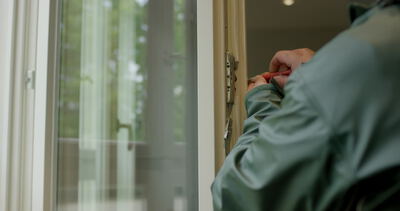 Nahaufnahme von einem Handwerker beim Justieren oder Reparieren von einem Fensterbeschlag mit einem Schraubendreher
