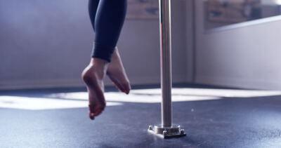 Person bei einer Gymnastikübung an einer vertikalen Stange im Trainingsraum