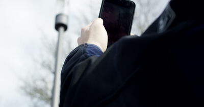 Person hält ein Smartphone in den Händen und fotografiert eine Straßenlaterne im Freien