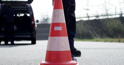 Person in Arbeitskleidung stellt Pylon auf asphaltierter Straße ab