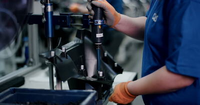 Person verschraubt ein schwarzes Kunststoffbauteil mit einem Elektrowerkzeug in einer Fabrik Person verschraubt ein schwarzes Kunststoffbauteil mit einem Elektrowerkzeug in einer Fabrik, Montage, Fertigung und