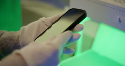 Prüfung eines Smartphones durch eine Fachkraft mit weißen Handschuhen in einem Labor