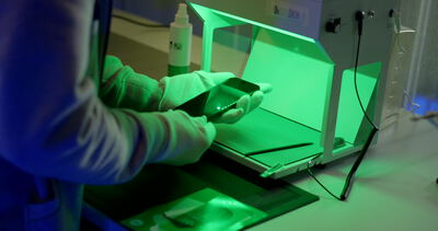 Reinigung eines Smartphones unter einer speziellen Lichtquelle in einem Techniklabor