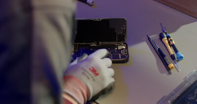 Reparatur eines geöffneten Smartphones mit Feinmechanik-Werkzeug am Arbeitstisch