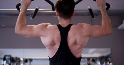 Rückansicht eines Mannes beim Krafttraining mit Klimmzügen an einer Klimmzugstange im Fitnessstudio