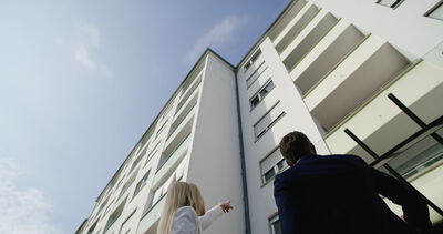 Rückansicht von einem Paar im Business-Outfit beim Betrachten von einer modernen Wohnhausfassade aus der Froschperspektive
