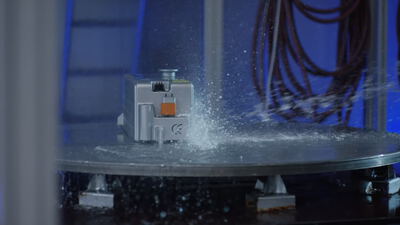 Silberner Lithium-Ionen-Akku bei einem Spritzwasser-Belastungstest auf einem rotierenden Drehteller