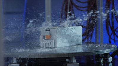Silberner Lithium-Ionen-Akku bei einem Spritzwasser-Belastungstest auf einem rotierenden Drehteller