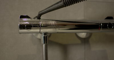 Dampfreiniger poliert Chromarmatur einer Dusche im Bad