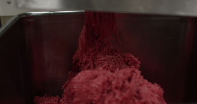 Frisches Hackfleisch fällt aus dem Fleischwolf in die Edelstahlwanne