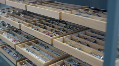 Zahlreiche Brillen liegen sortiert in Holzschubladen im Optikergeschäft